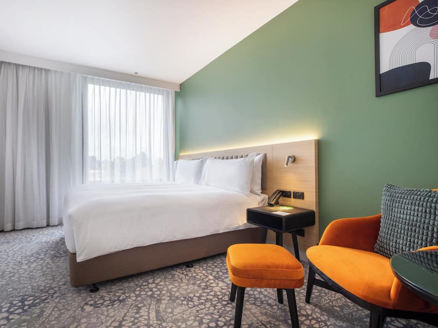 Una habitación de hotel con una cama, un escritorio, una silla naranja y un televisor.