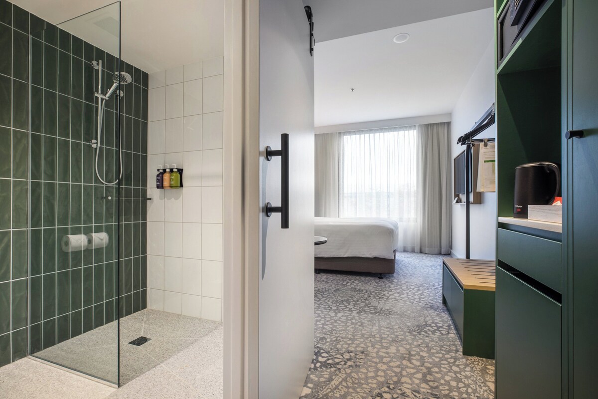 Habitación de hotel con ducha, cama, escritorio y armario.