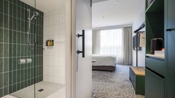 A hotel room with a shower, a bed, a desk, and a minibar.