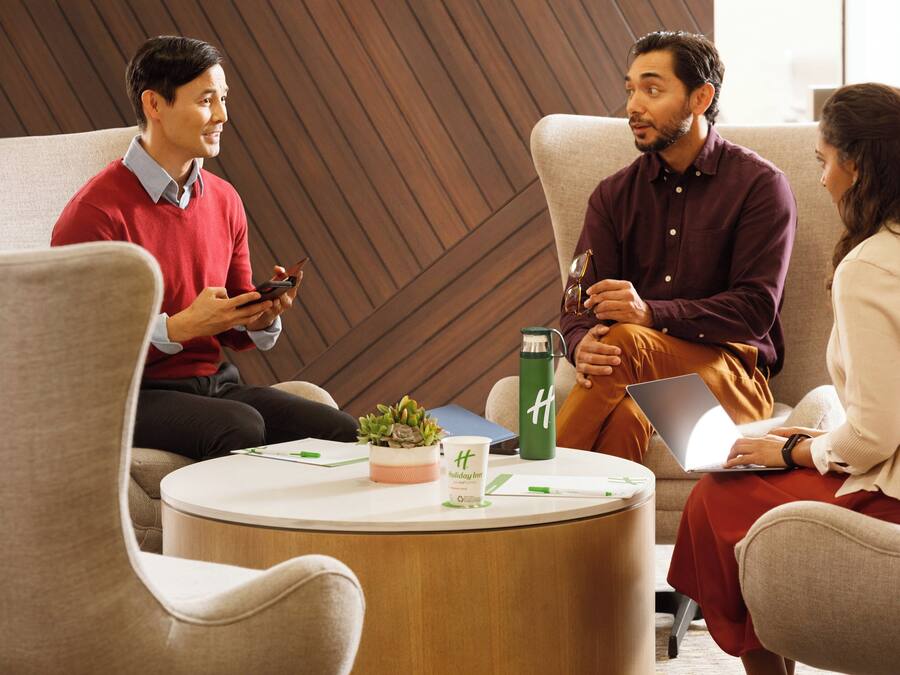 A group of people in a modern lounge area with a round table, a potted plant, and a water bottle.