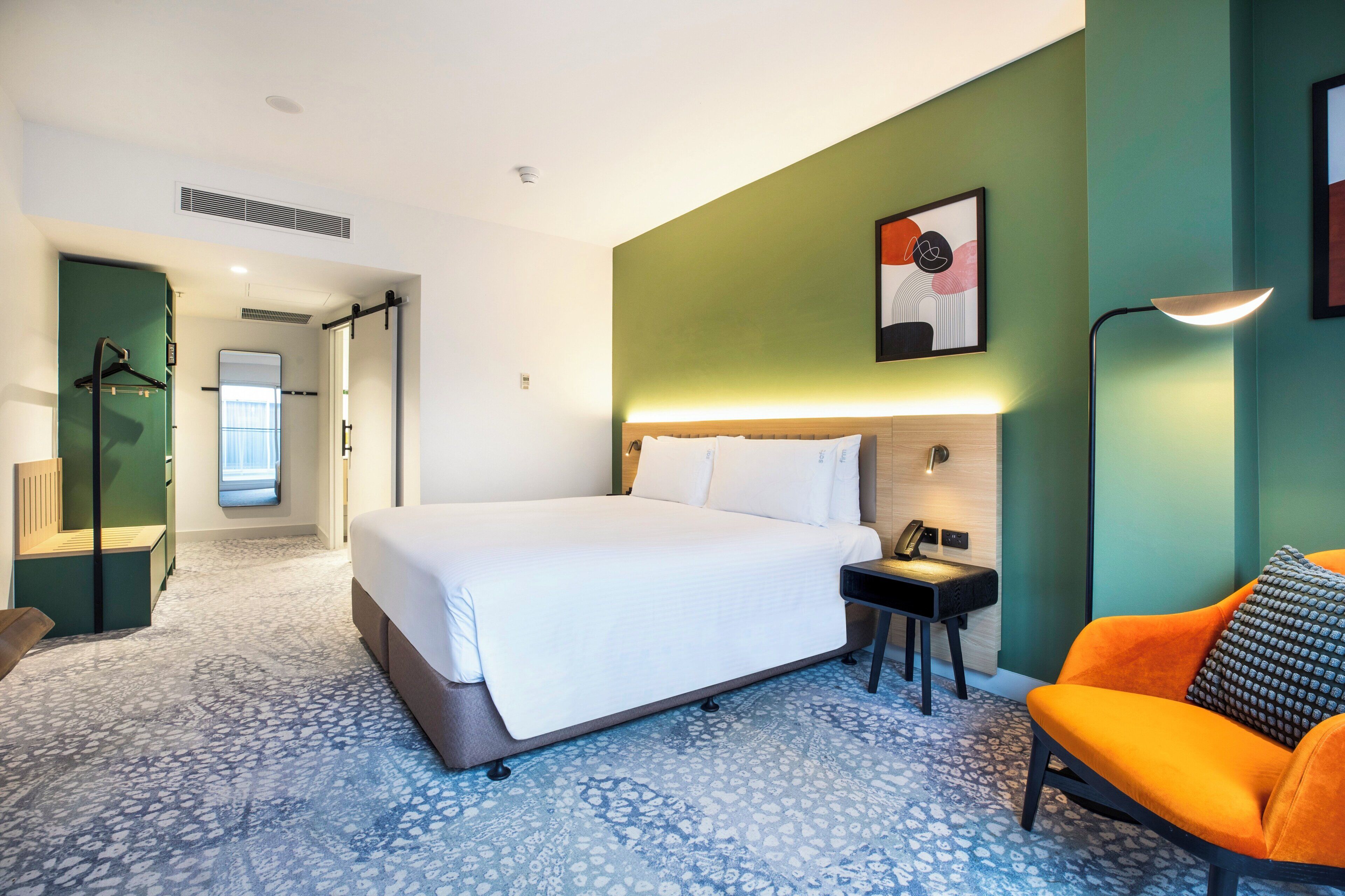 Een hotelkamer met een bed, een stoel, een bureau en een schilderij aan de muur.