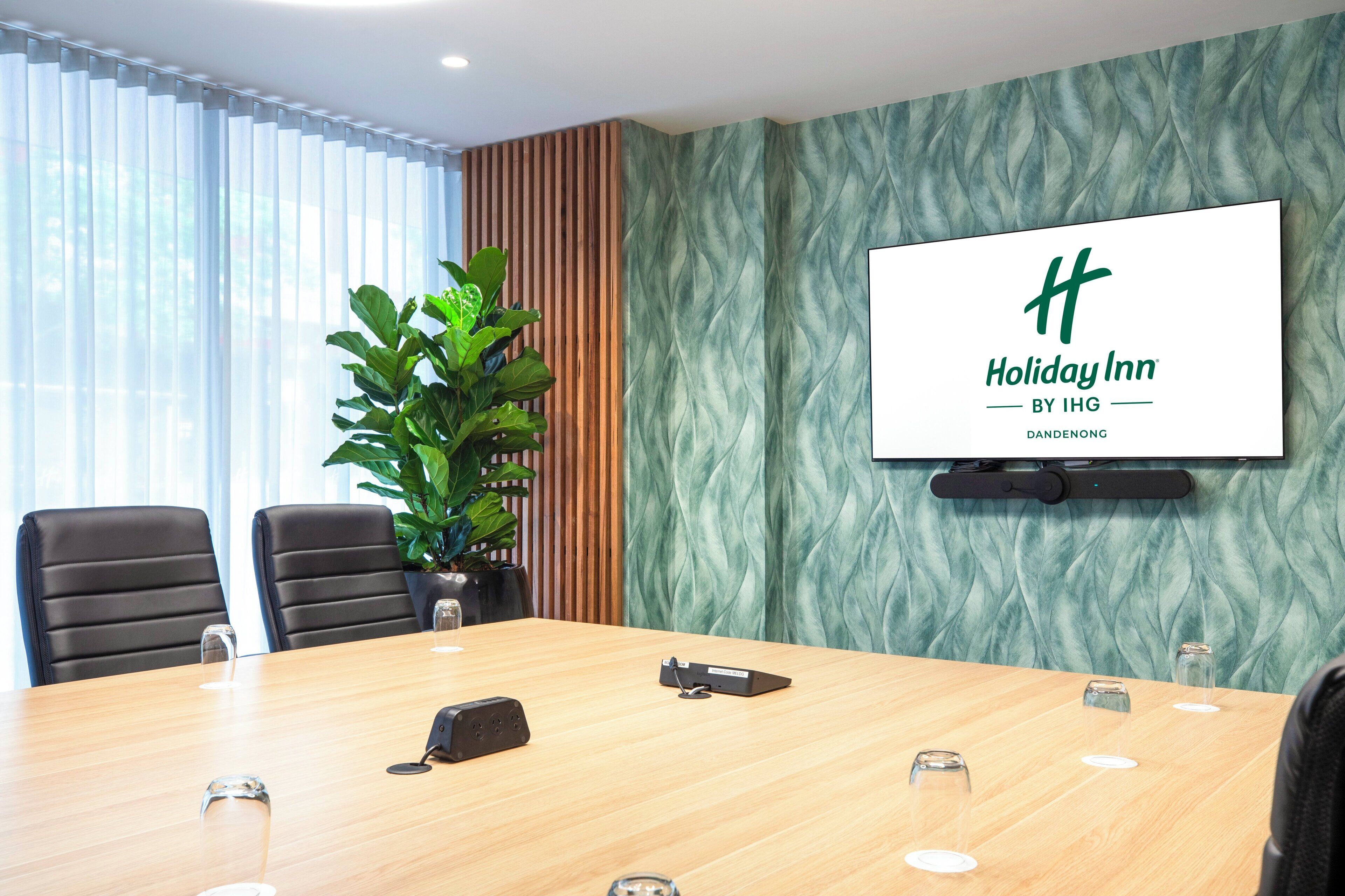 A conference room with a large table, chairs, a projector, and a screen displaying the Holiday Inn logo.