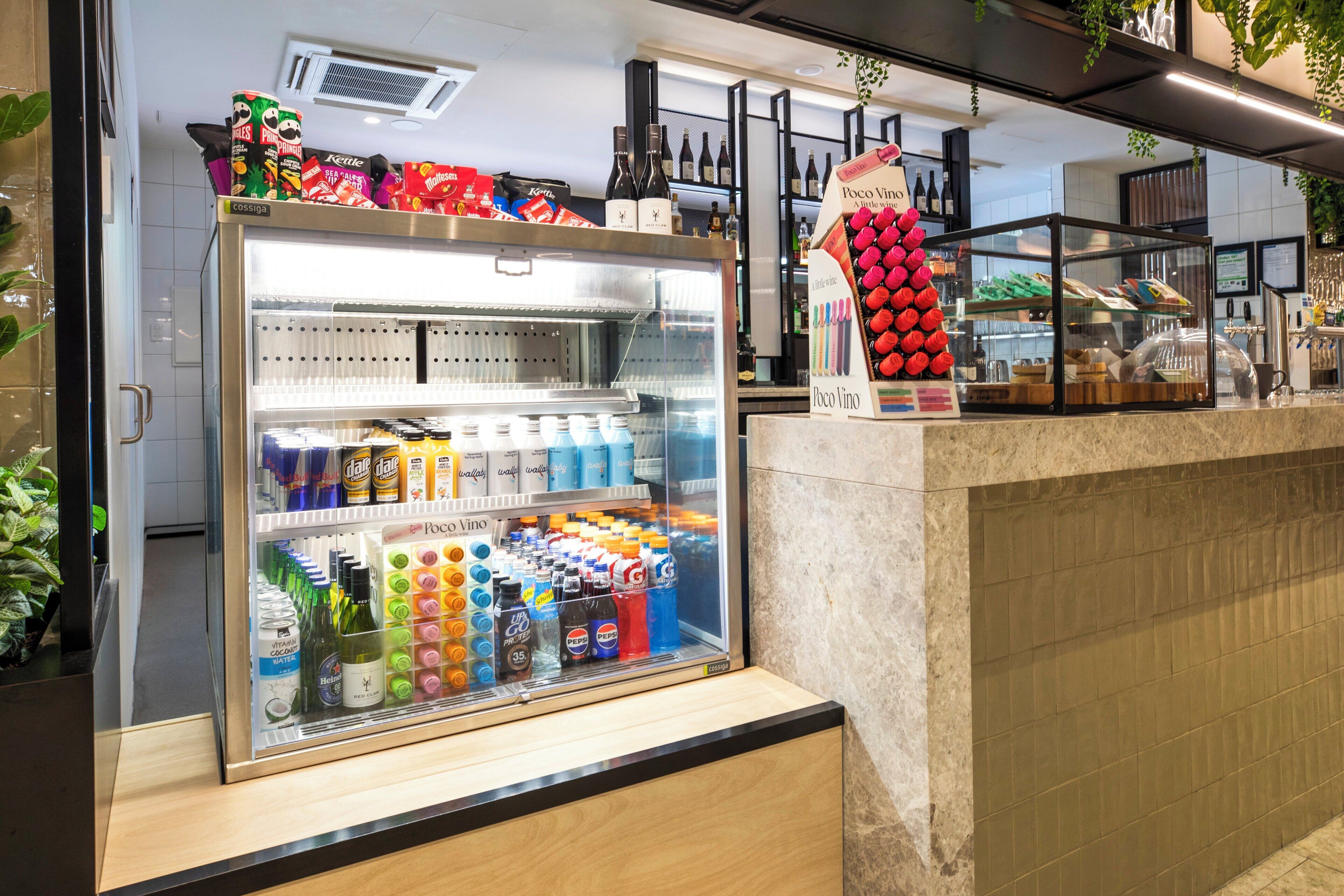 A refrigerated display case filled with various beverages and a promotional stand for Pocito Vino wine.