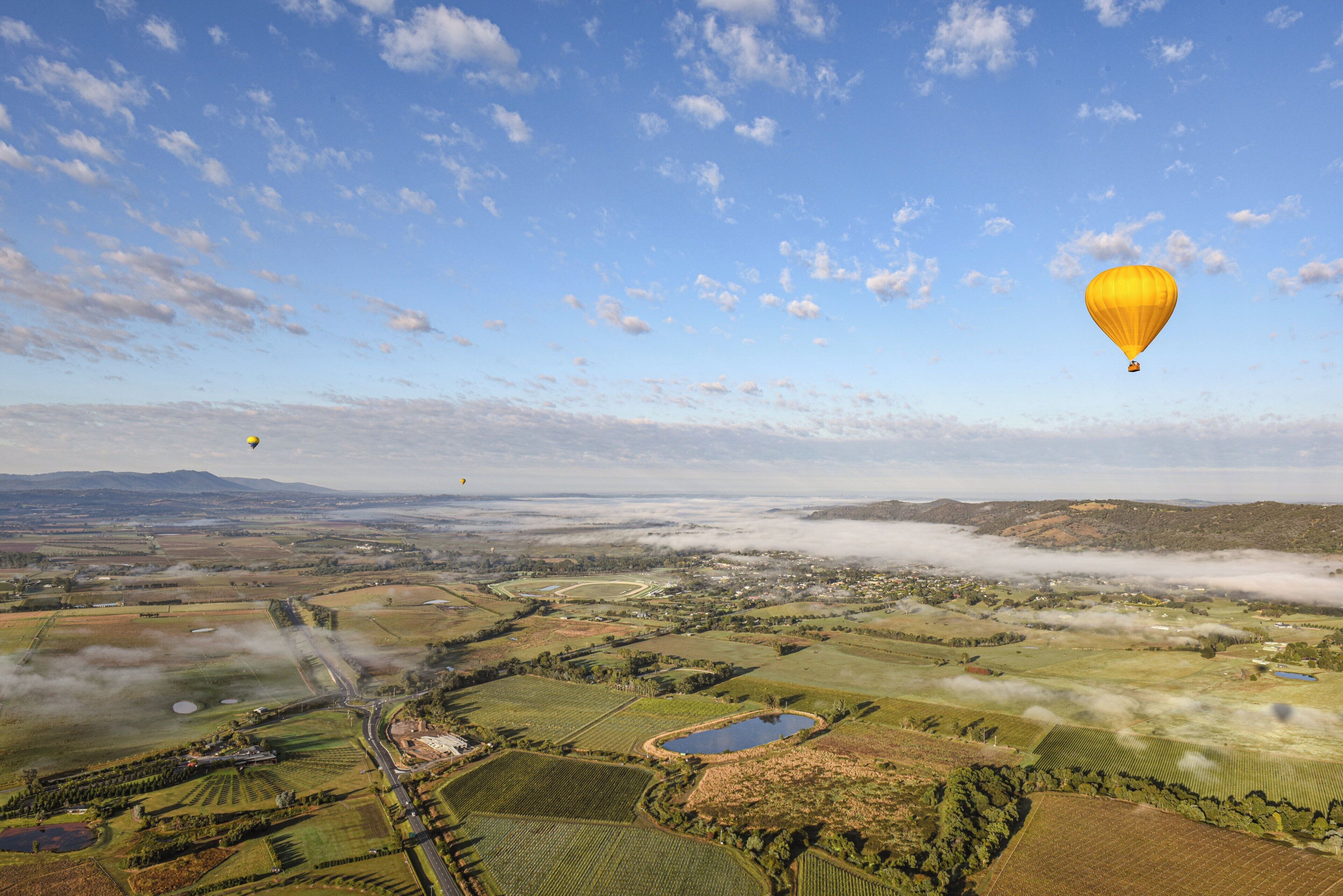 A hot air balloon over a rural landscape with fields, a small body of water, and a road.