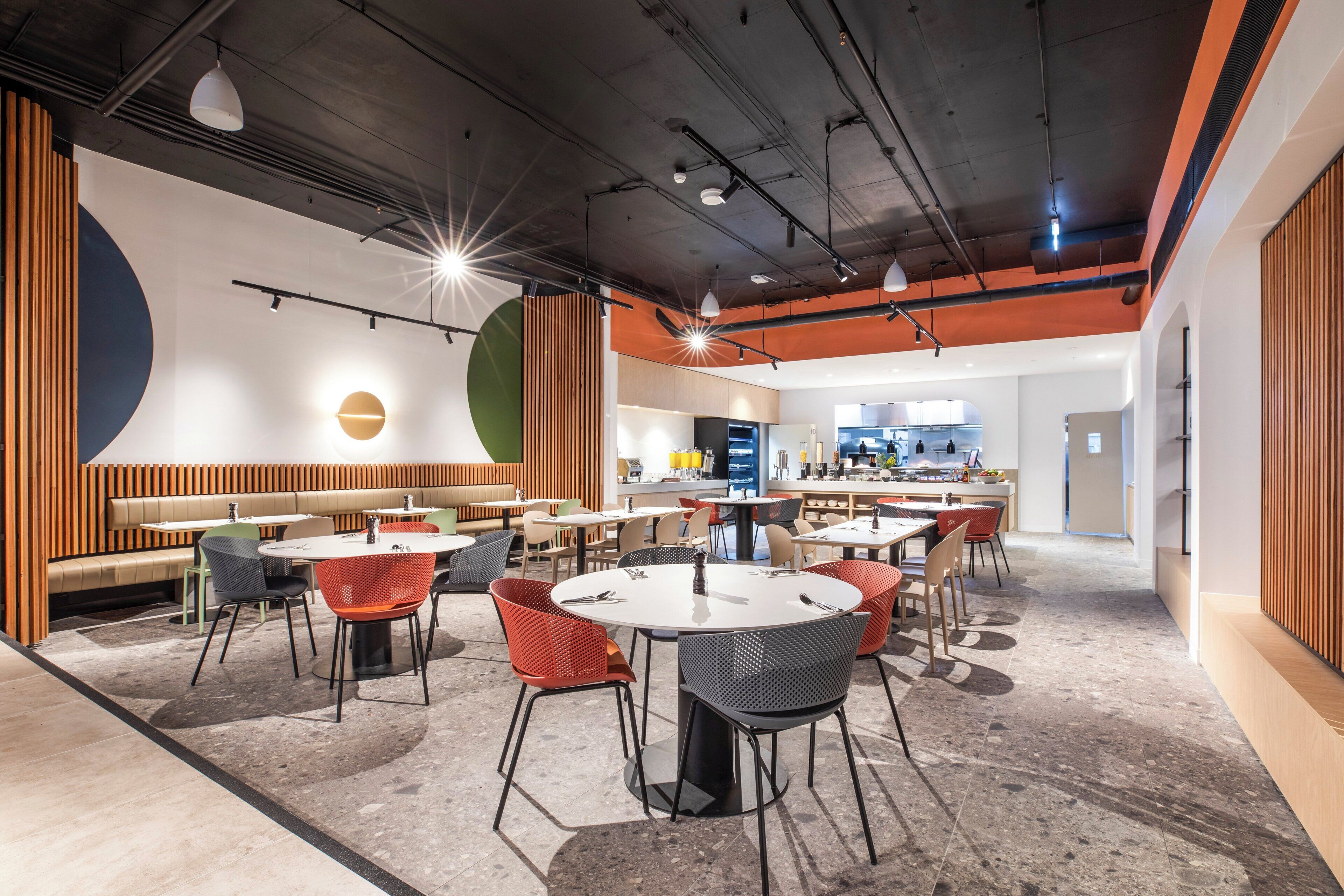 A modern dining area with round tables and chairs, a bar area, and a kitchen in the background.