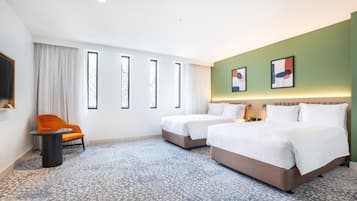 Habitación de hotel con dos camas, una silla, una mesita pequeña y un ventanal con cortinas.