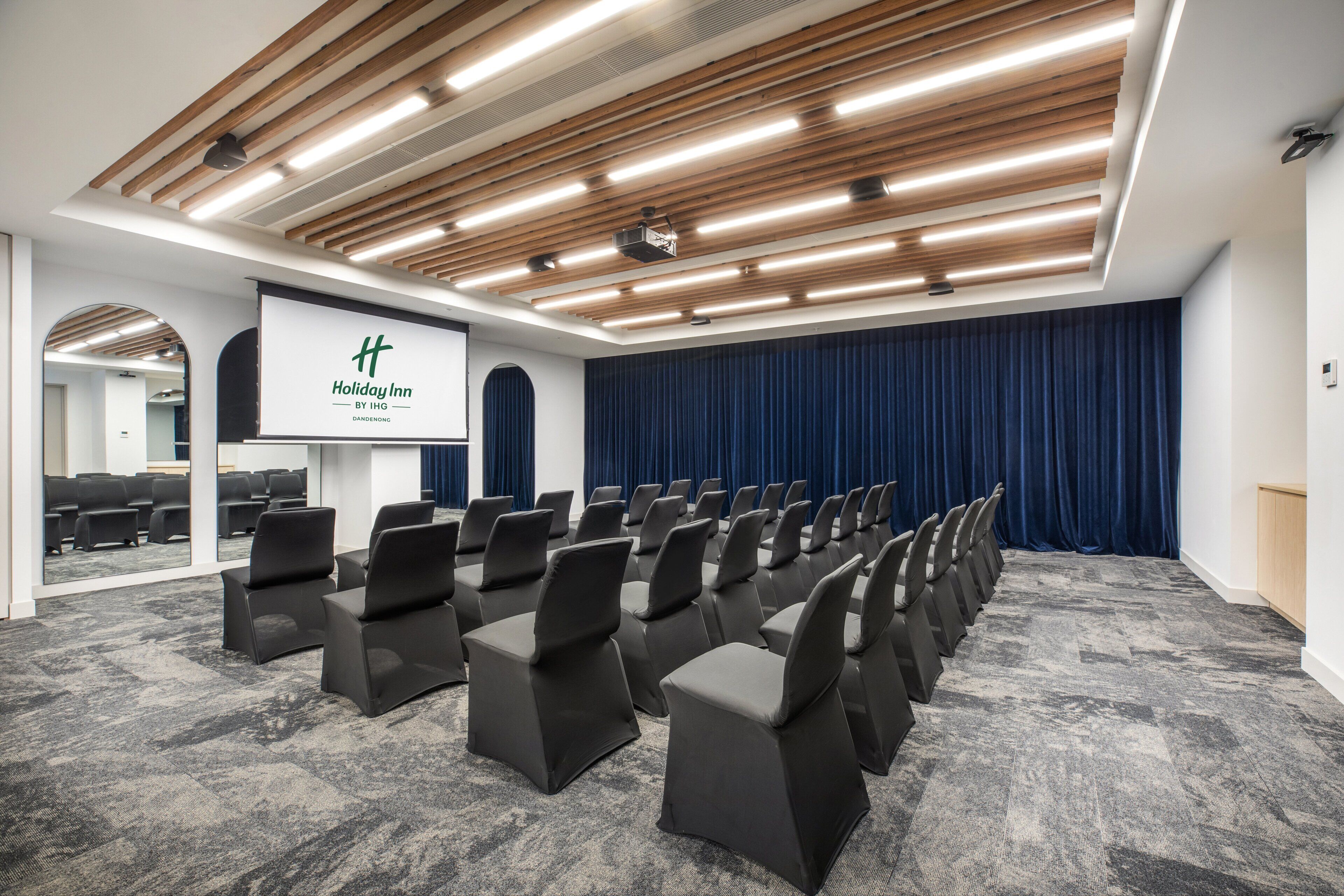 A conference room with rows of chairs, a podium, and a large screen.