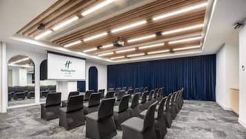 A conference room with rows of chairs, a podium, and a large screen.