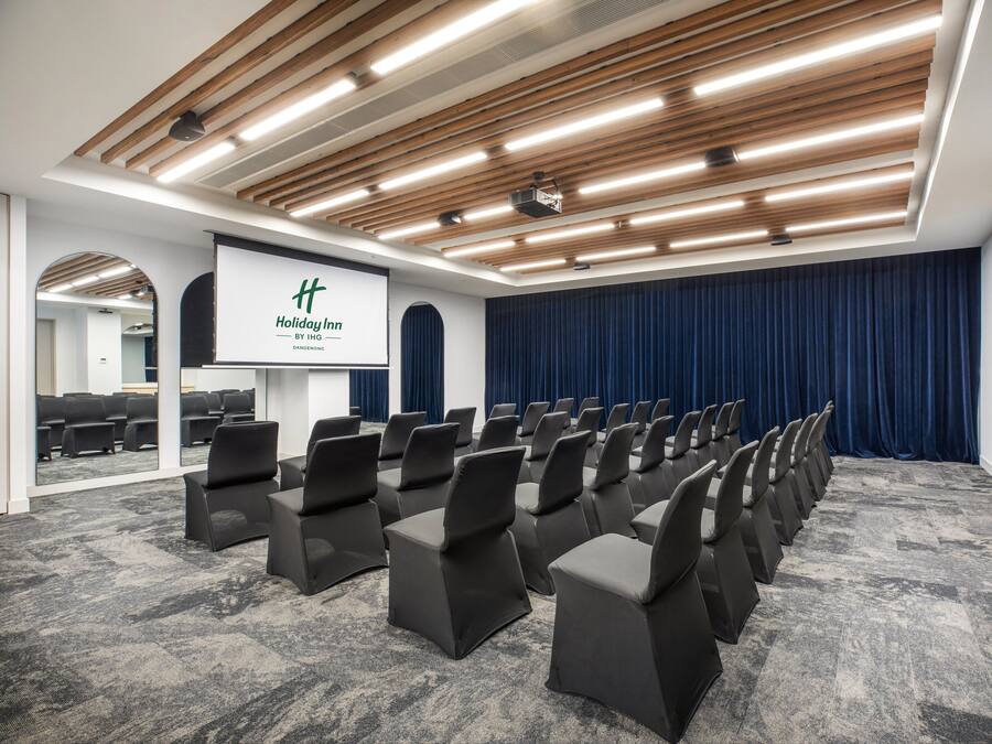 A conference room with rows of chairs, a podium, and a large screen.