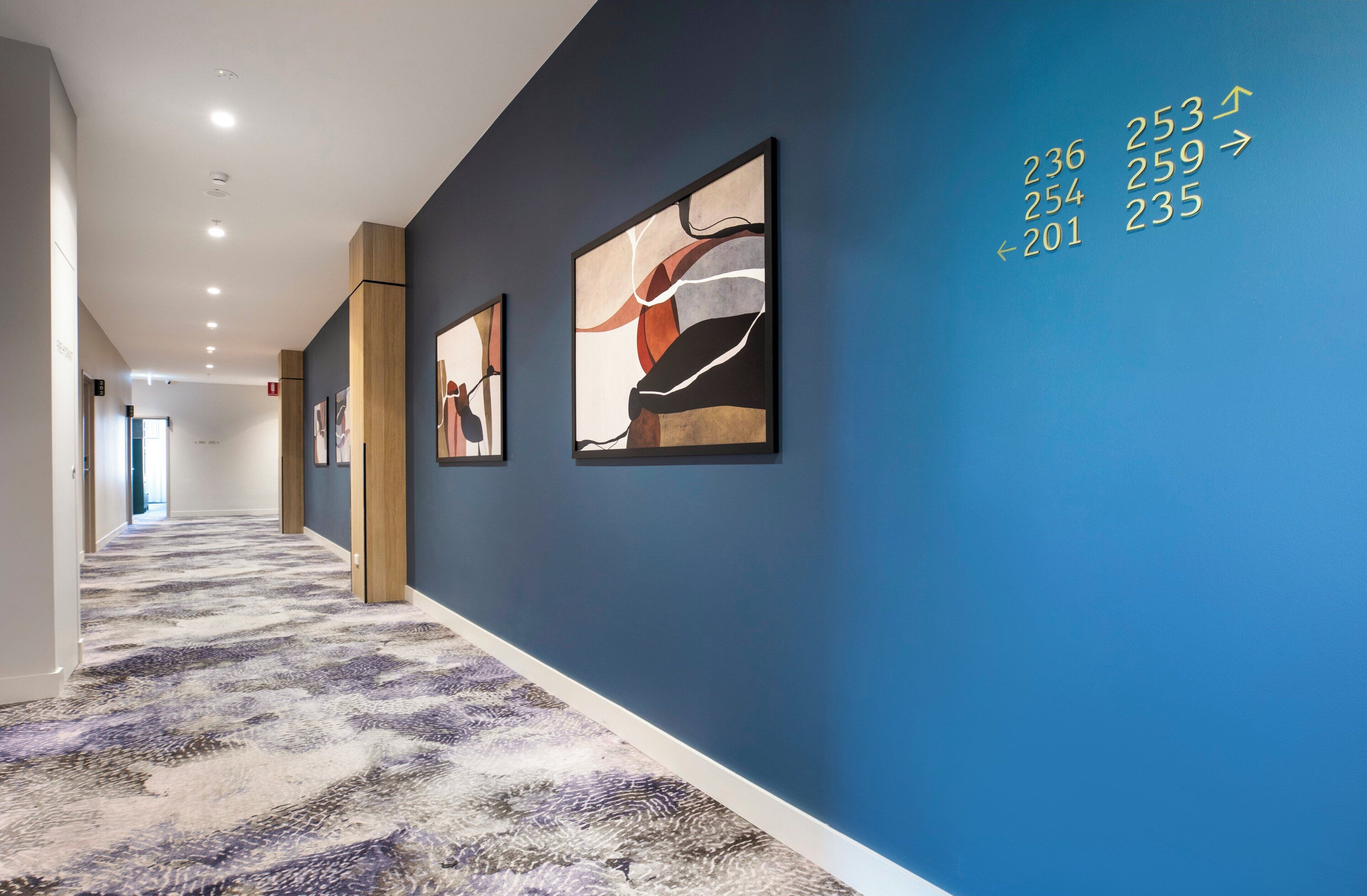 A hallway with a patterned carpet, blue walls, and abstract art.