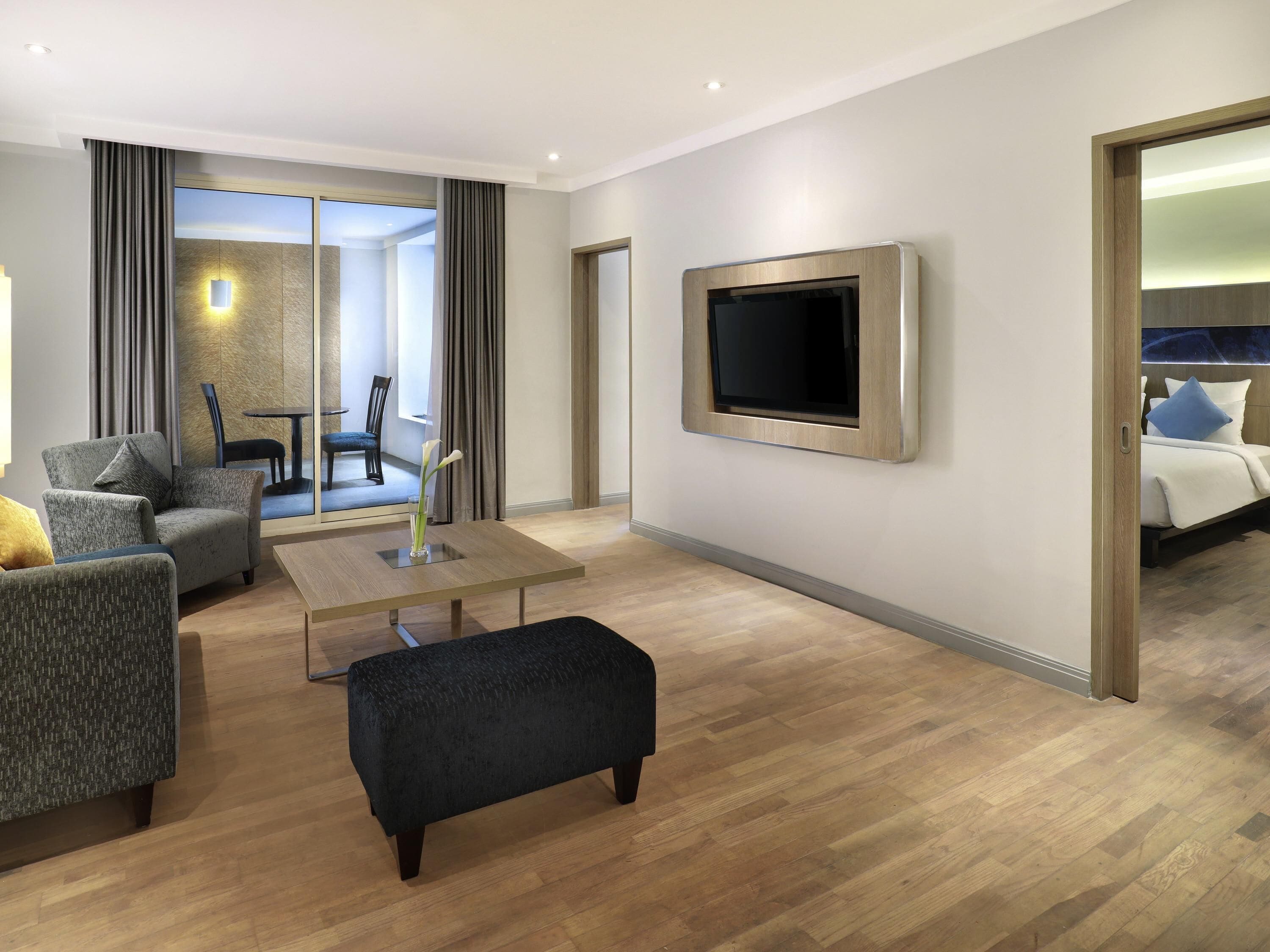 A modern hotel room with a flat-screen TV, a sofa, a coffee table, and a bed with pillows.