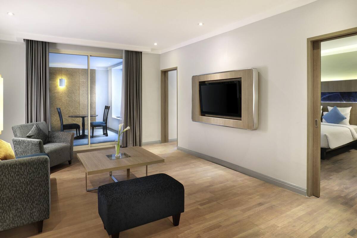 A modern hotel room with a flat-screen TV, a sofa, a coffee table, and a bed with pillows.