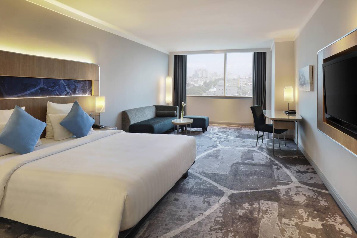 A hotel room with a large bed, a sofa, a desk, and a TV.