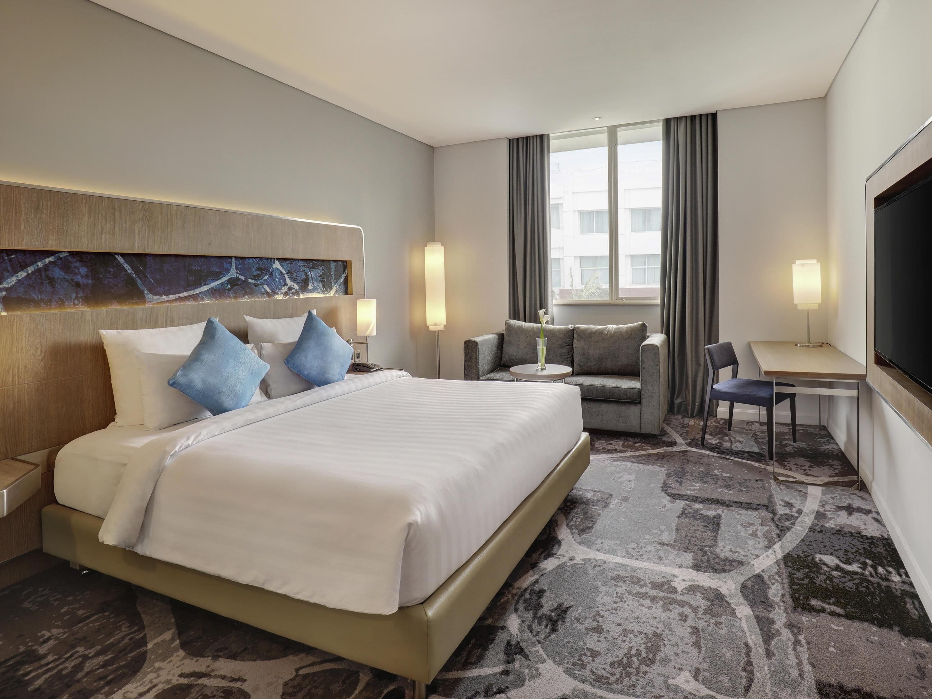A hotel room with a large bed, a sofa, a desk, and a TV.