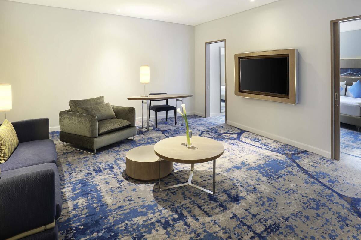 A hotel room with a sofa, a small table with a candle, a TV, and a carpeted floor.