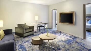 A hotel room with a sofa, a small table with a candle, a TV, and a carpeted floor.