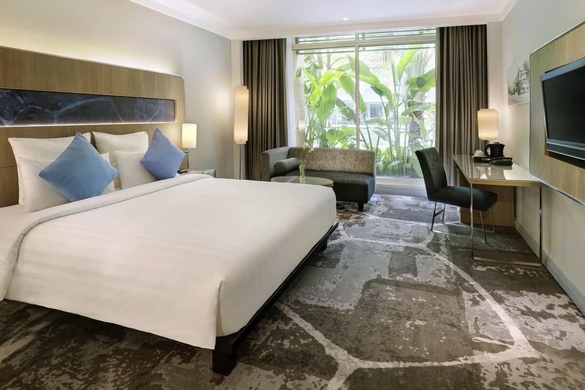 A hotel room with a large bed, a desk, a chair, and a TV.
