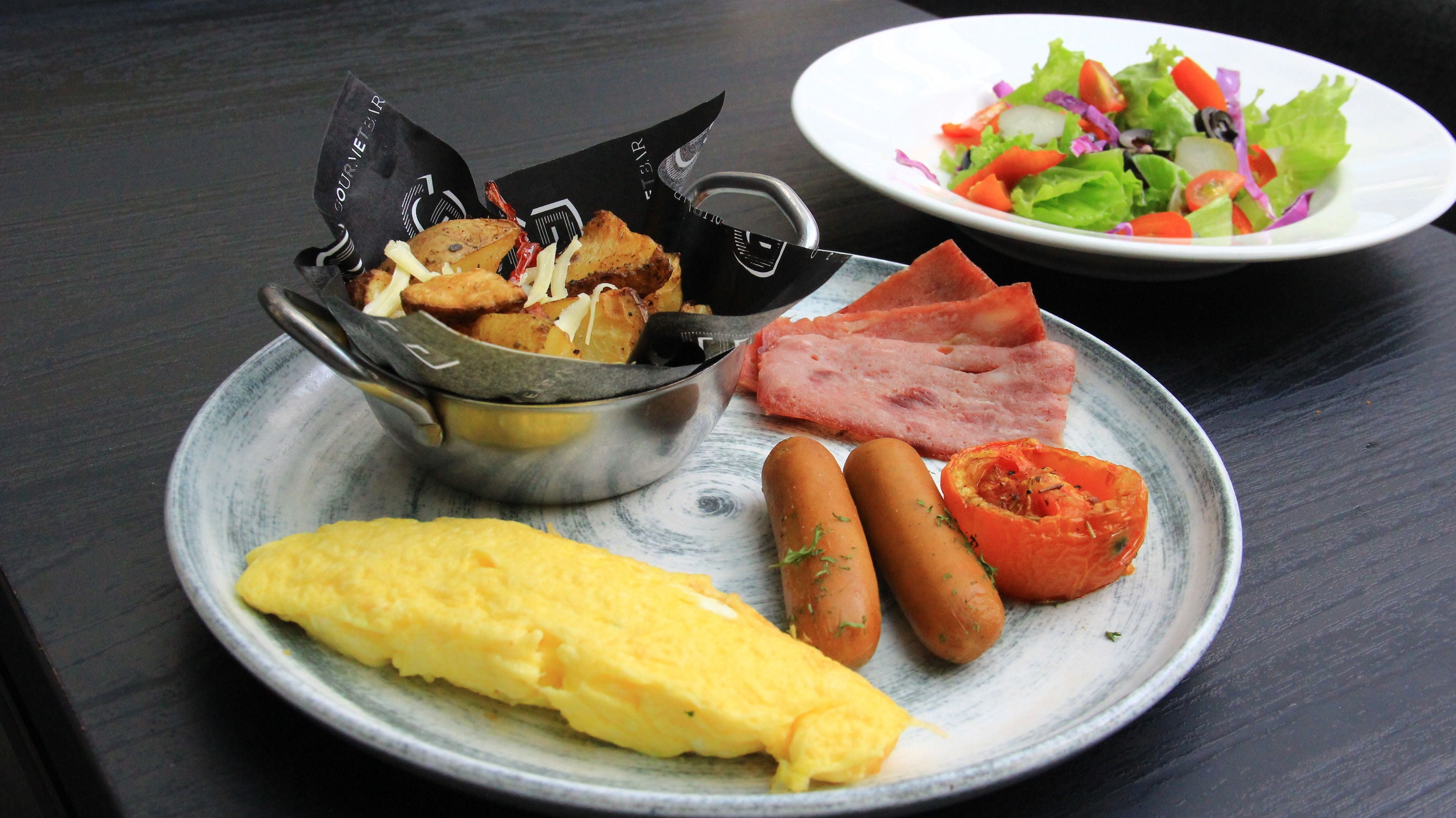 Une assiette avec une omelette, des saucisses, du jambon et une salade.