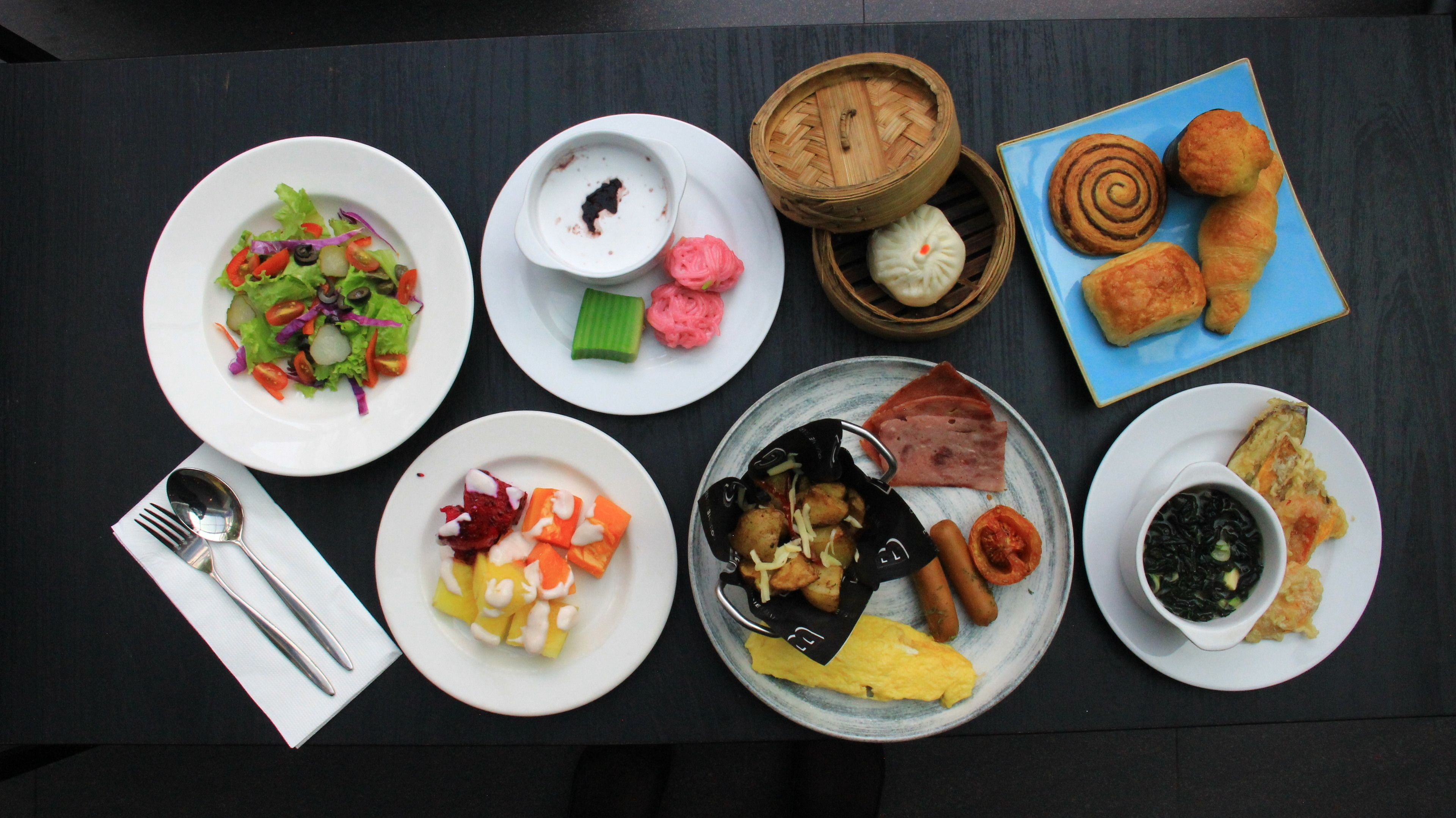 Una mesa con diversos platos, incluyendo una ensalada, dumplings, pasteles y un plato con huevos y salchichas.