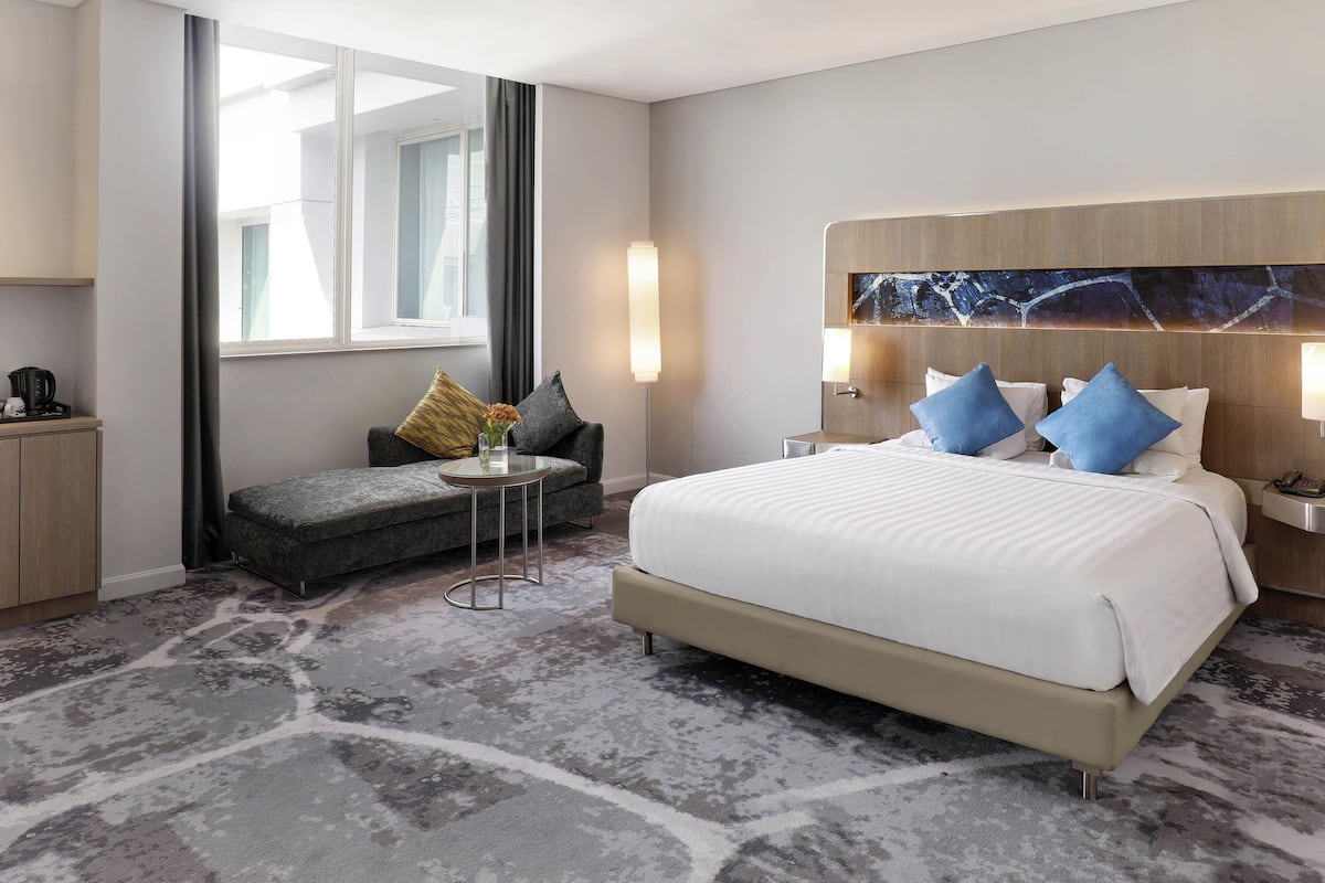 Ein Hotelzimmer mit Bett, Sofa, kleinem Tisch, Lampe und Blick ins Freie.