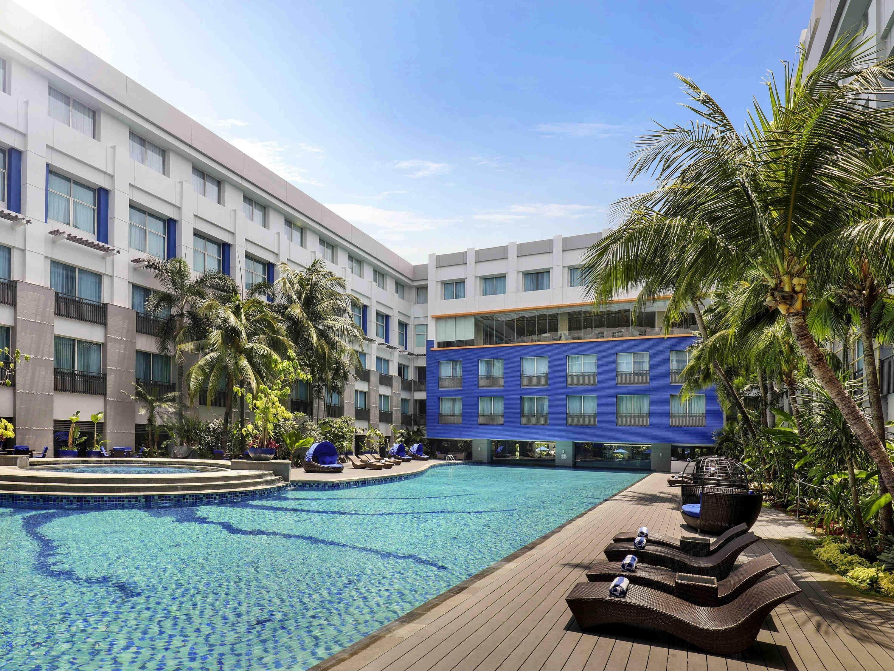 A hotel with a swimming pool, palm trees, and a blue building.