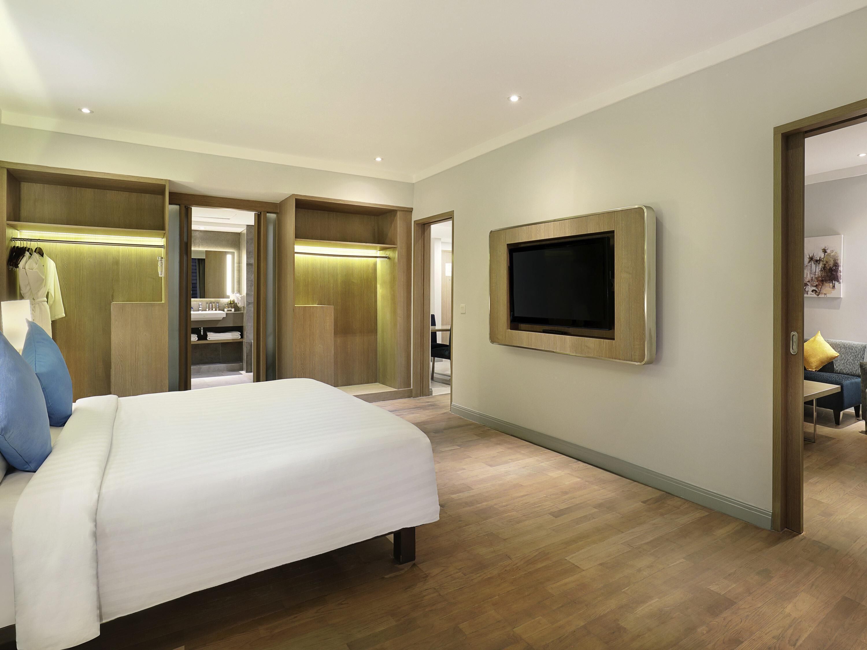 A hotel room with a bed, a TV mounted on the wall, a walk-in closet, and a bathroom.