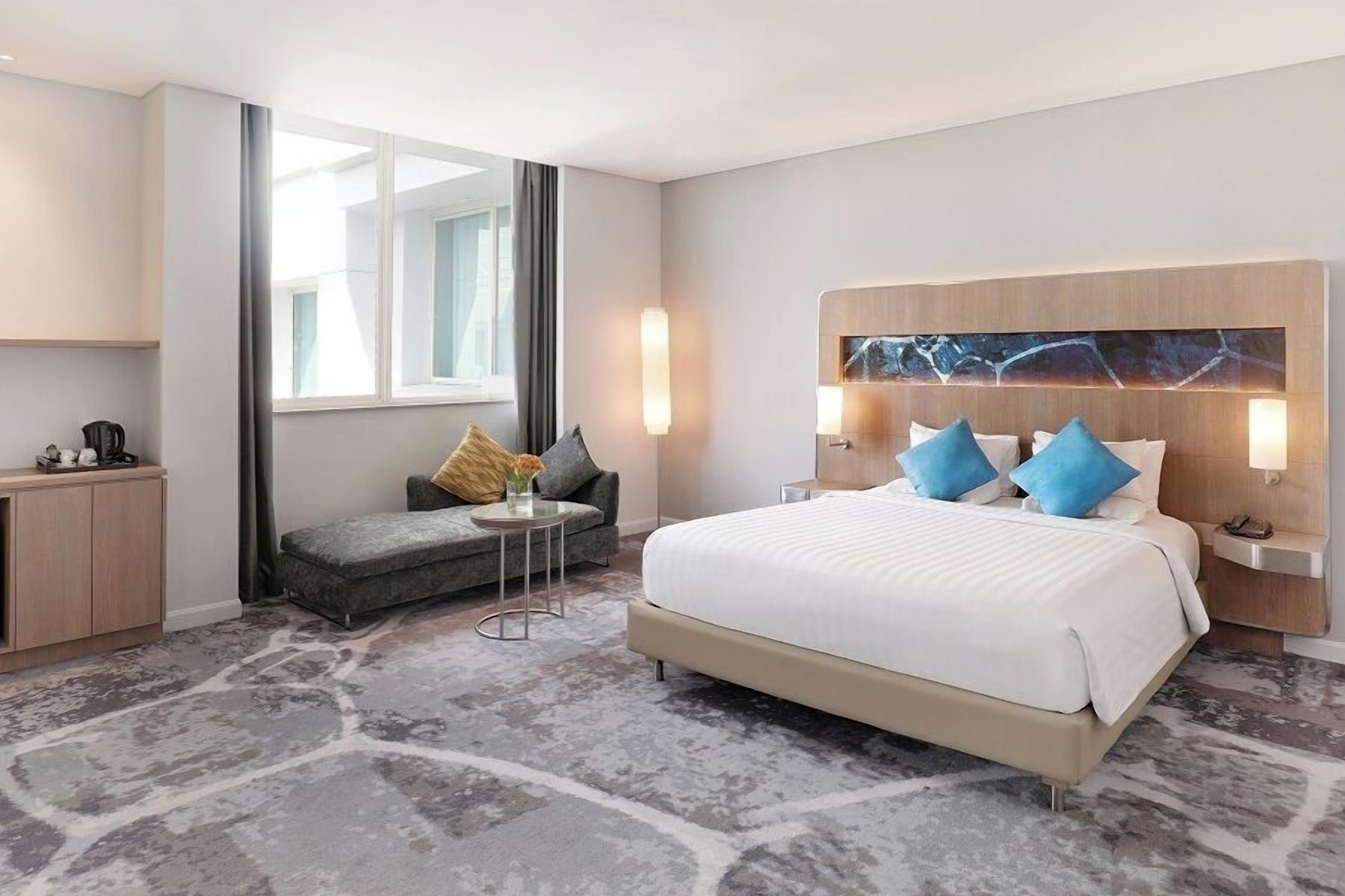 A modern hotel room with a large bed, a sofa, a small table, and a desk.