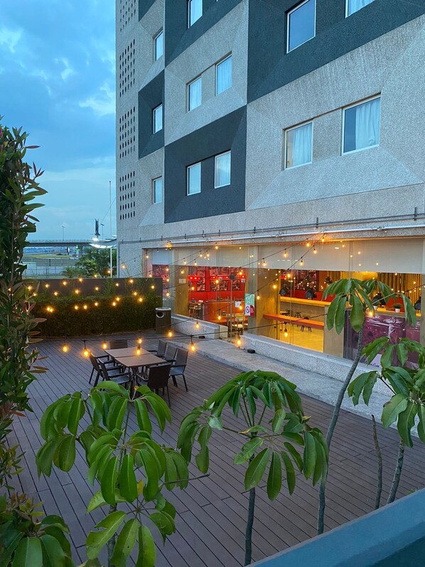 Un edificio moderno con terraza en la azotea, que cuenta con asientos exteriores e iluminación con guirnaldas.