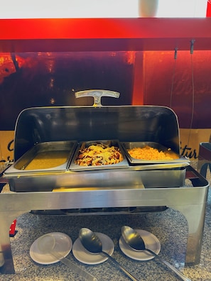 A buffet setup with two serving trays, a spoon on a plate, and a metal tongs holder.