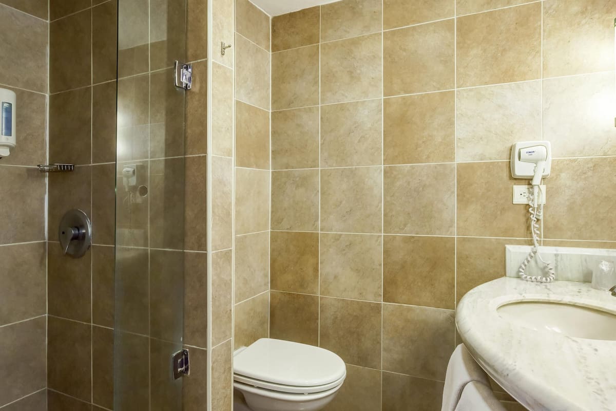 Un baño con baldosas color crema, cabina de ducha de vidrio, inodoro y lavamanos con toalla.