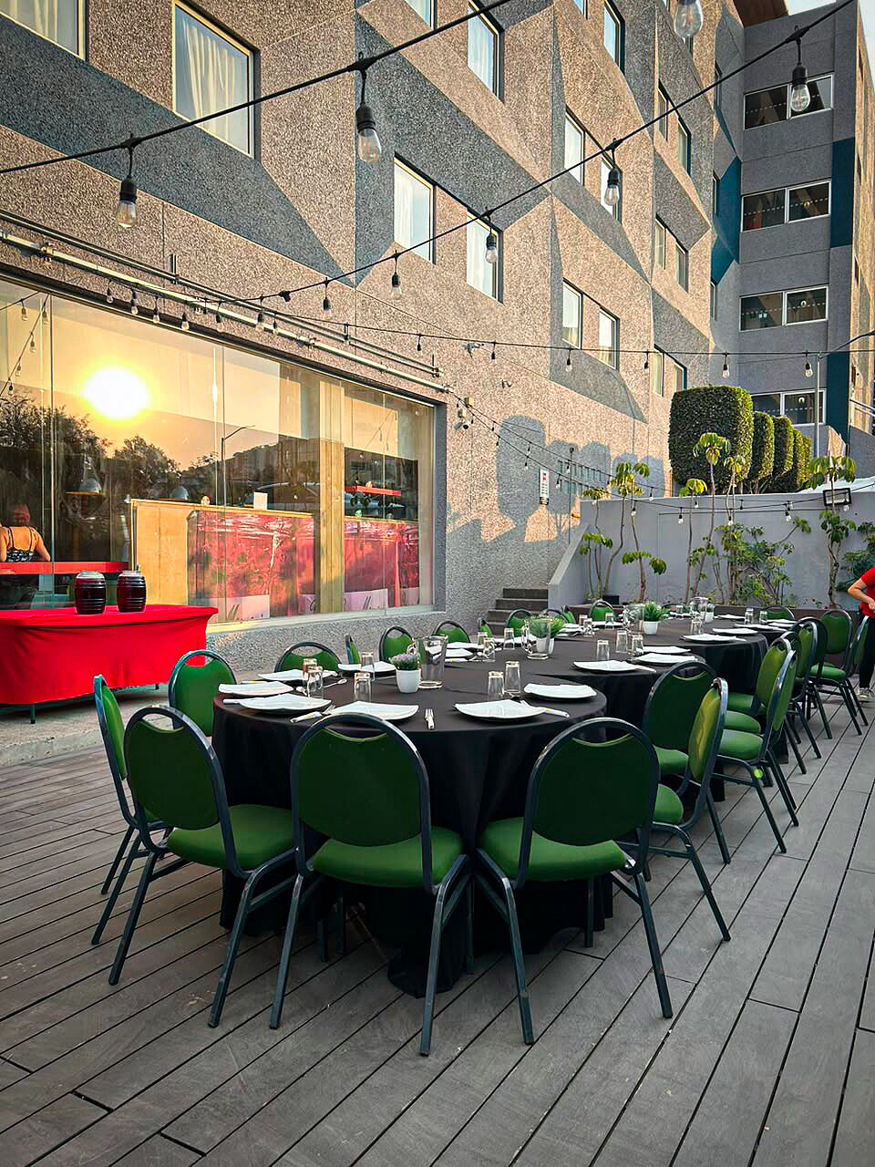 An outdoor dining area with tables and chairs, a red table, and a building with a geometric facade.