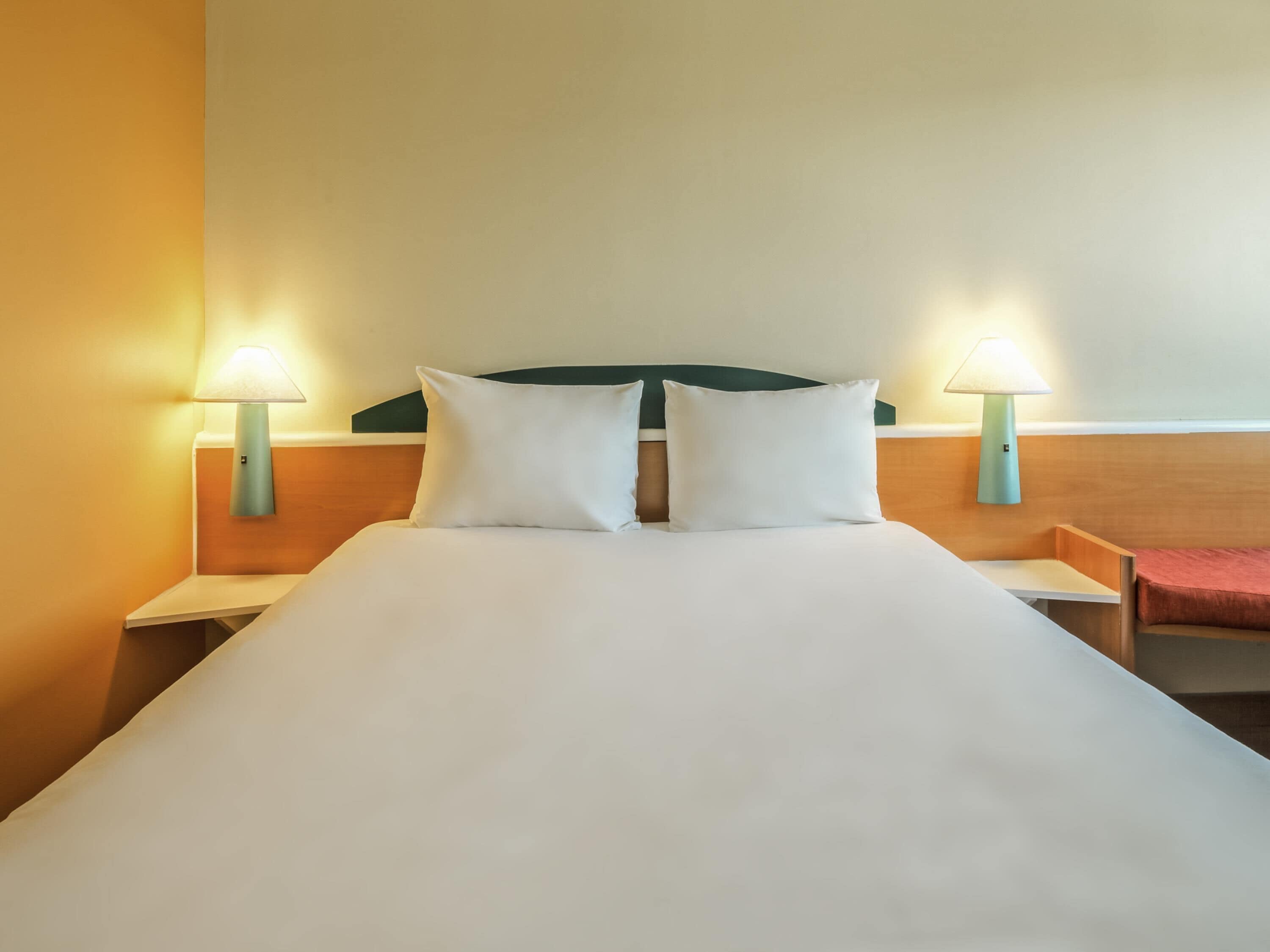 A hotel room with a bed, two bedside lamps, and a nightstand.