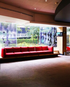 A red sofa in a lobby with a large window, a wooden column, and a directional sign.