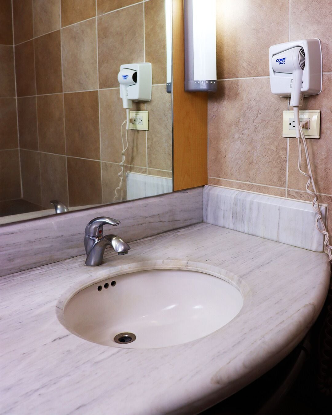 Un baño con lavamanos de mármol, un espejo y un secador de pelo montado en la pared.