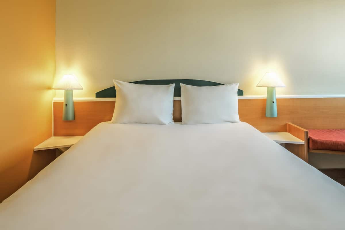 A hotel room with a large bed, two bedside lamps, and a wooden headboard.