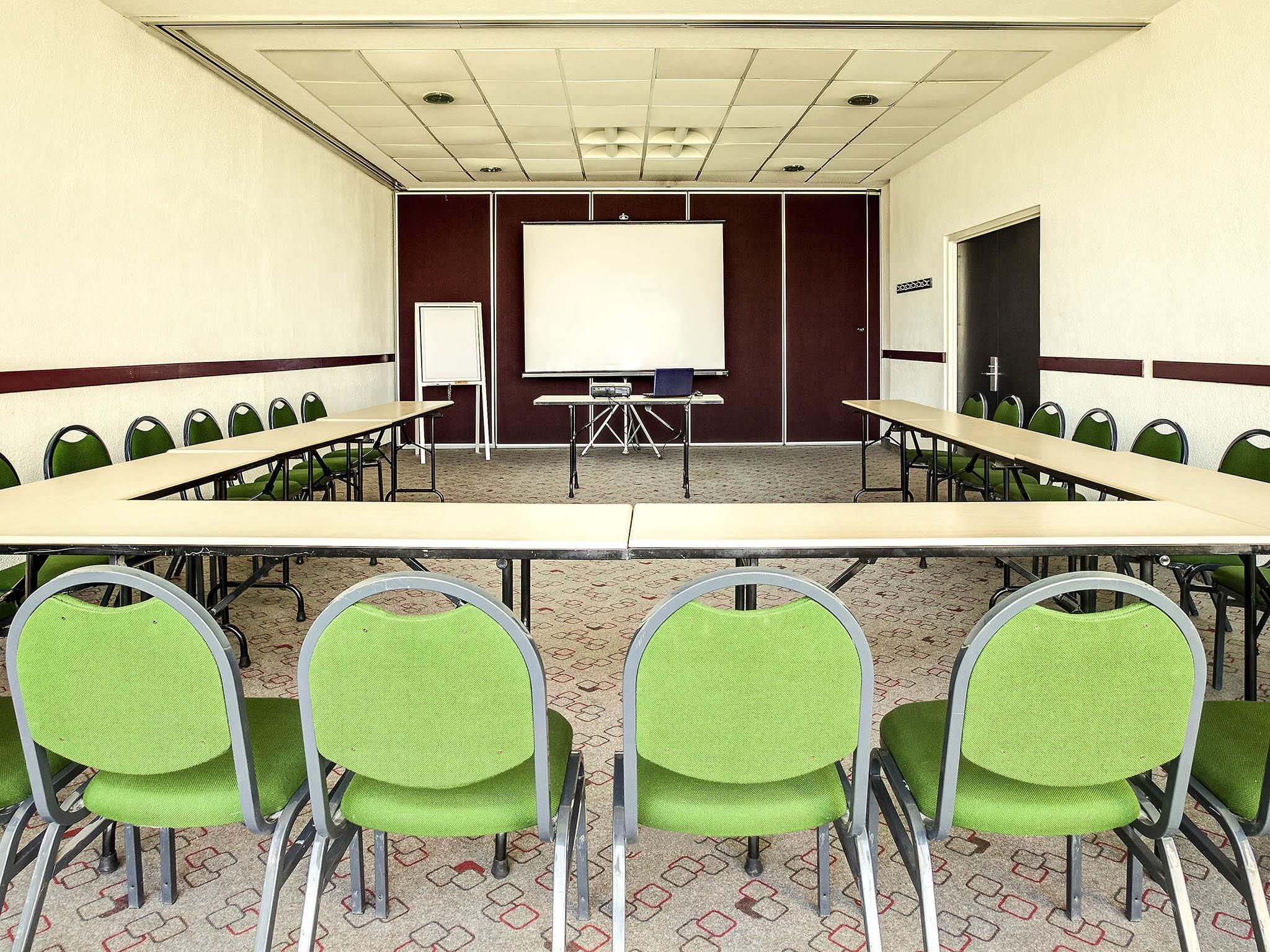 A conference room with a long table, green chairs, a whiteboard, and a projector.