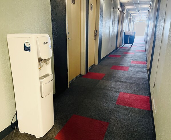 A hotel corridor with a water dispenser, doors, and a carpeted floor with red squares.