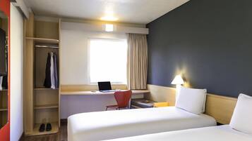 Habitación de hotel con dos camas, un escritorio con una computadora portátil, una silla, un armario y una ventana con cortinas.