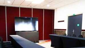 A conference room with a large flat-screen TV, rows of chairs, a long table, and a door with an emergency exit sign. - ibis Mexico Perinorte (Cuautitlan Izcalli)