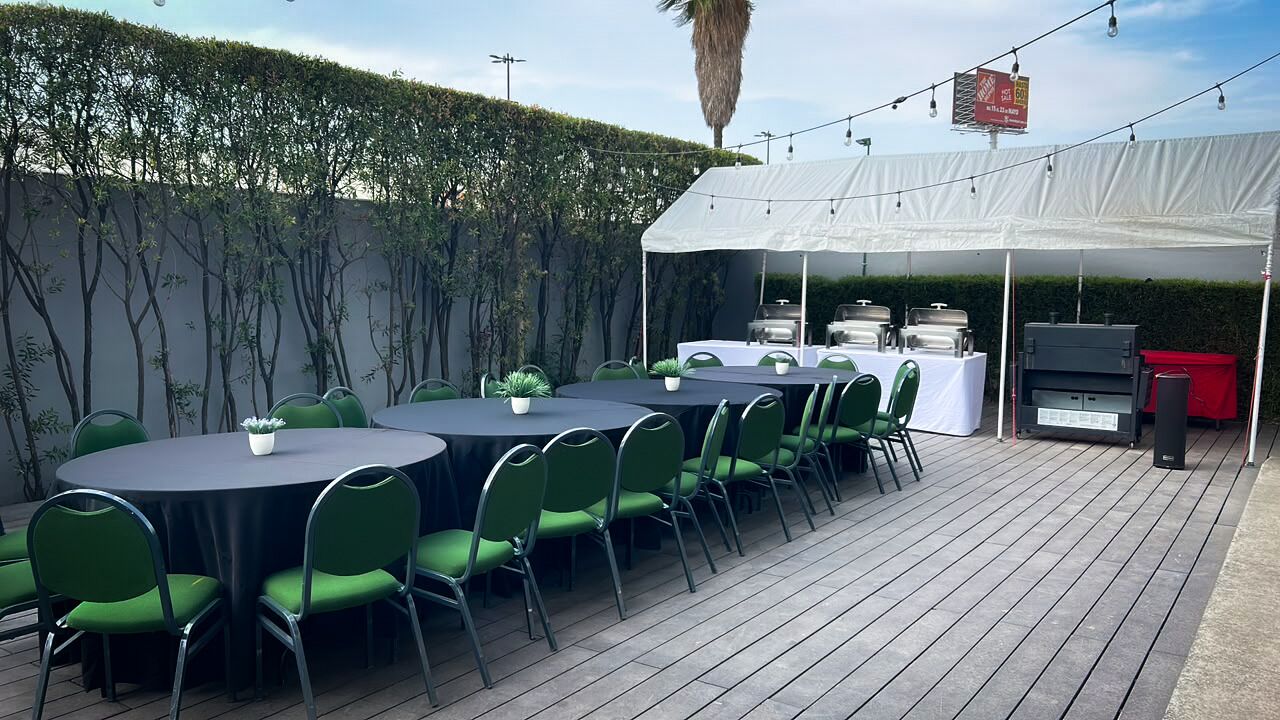 An outdoor patio with round tables and green chairs, a grill, and a white tent.