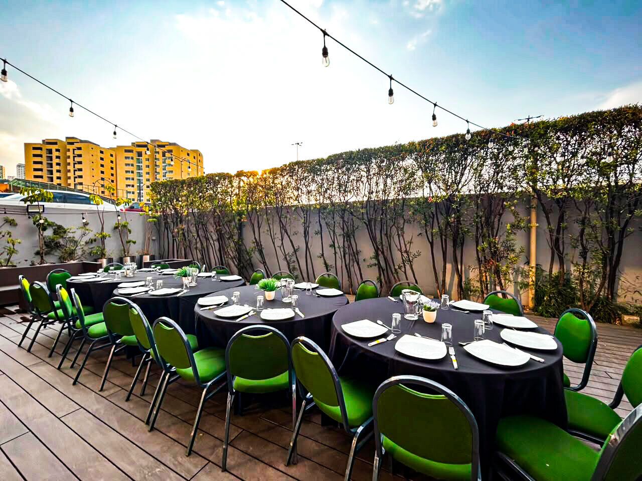 Un espace extérieur aménagé pour les repas, avec des tables rondes, des chaises vertes et des guirlandes lumineuses.