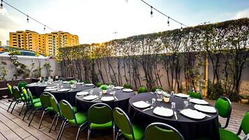 Un espace extérieur aménagé pour les repas, avec des tables rondes, des chaises vertes et des guirlandes lumineuses.
