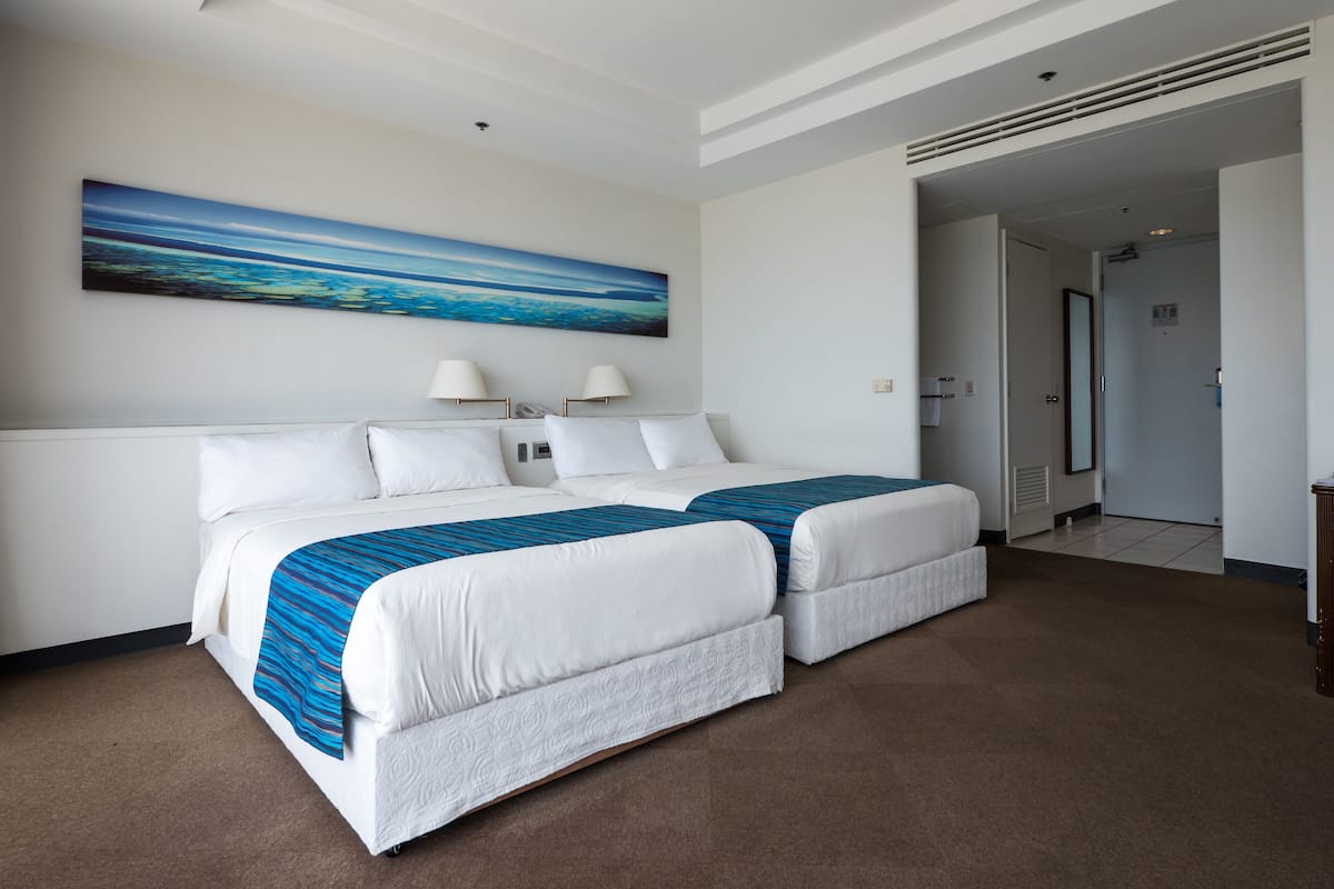 A hotel room with a large bed, two bedside lamps, a painting on the wall, and a door leading to another room.