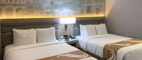 Habitación de hotel con dos camas, una mesita de noche con lámpara y un mural en la pared que representa el centro de Chico.