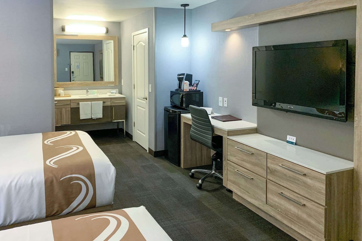 A hotel room with a bed, a desk, a television, a mirror, and a bathroom with a sink and towel.