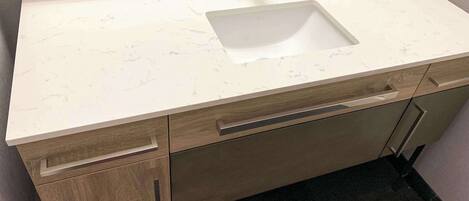 A bathroom with a marble countertop, a sink, and wooden cabinetry.