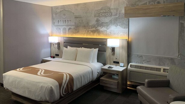 Een hotelkamer met een groot bed, nachtlampjes, een klein tafeltje, een sofa en een muur met een muurschildering.
