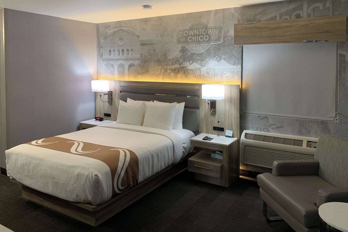 A hotel room with a large bed, bedside lamps, a small table, a sofa, and a wall with a mural.