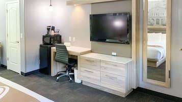 Habitación de hotel con cama, escritorio, televisor de pantalla plana, silla y pequeña zona de kitchenette.