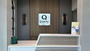 Een receptiebalie met een 'Quality by Choice Hotels' bord, een houten paneel en een klein informatiebord.